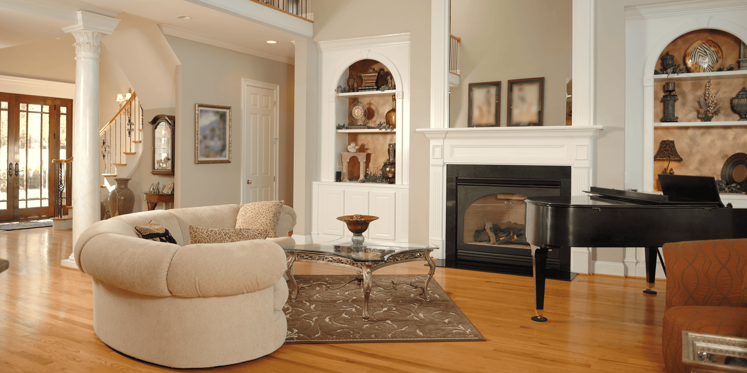 Elegant home interior with curved beige sofa, grand piano, fireplace, and built-in wall shelving in a traditional style